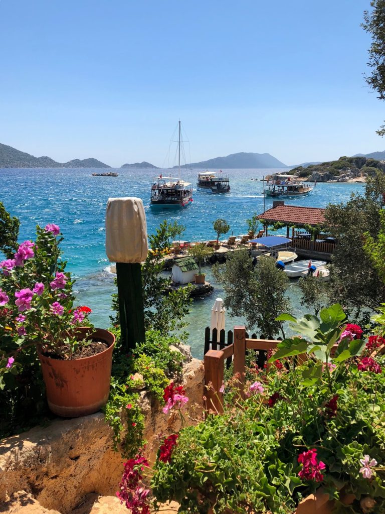 Bunte Blumen auf einer Terrasse und im Hintergrund das Meer mit Booten