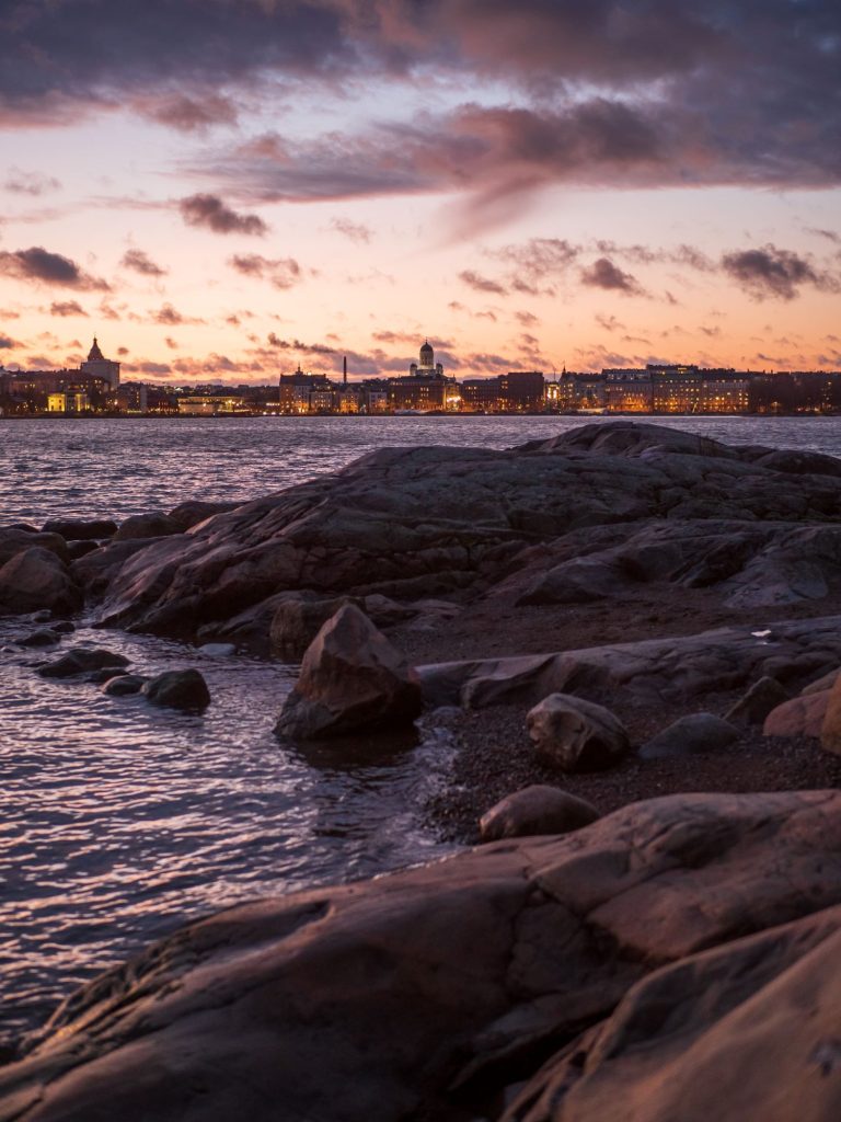 Felsige Küste bei Sonnenuntergang mit der Skykine von Helsinki im Hintergrund