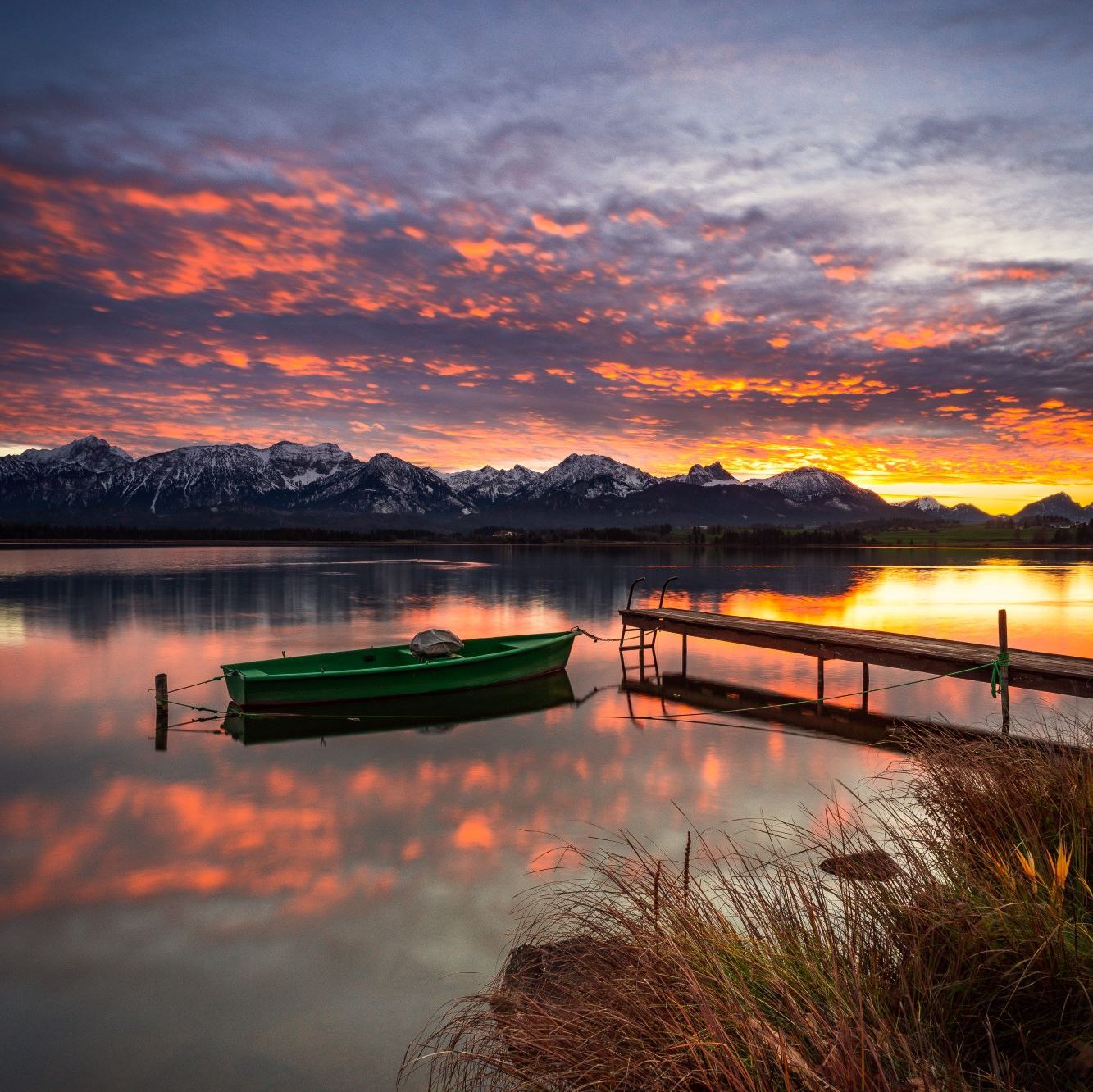 Hopfensee mit einem Steg und Boot beim Sonnenuntergang im Hintergrund sind Berge