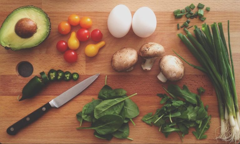 Camping-Rezepte Vegetarisch - Blick auf ein Schneidebrett mit viel Gemüse und einem Messer.