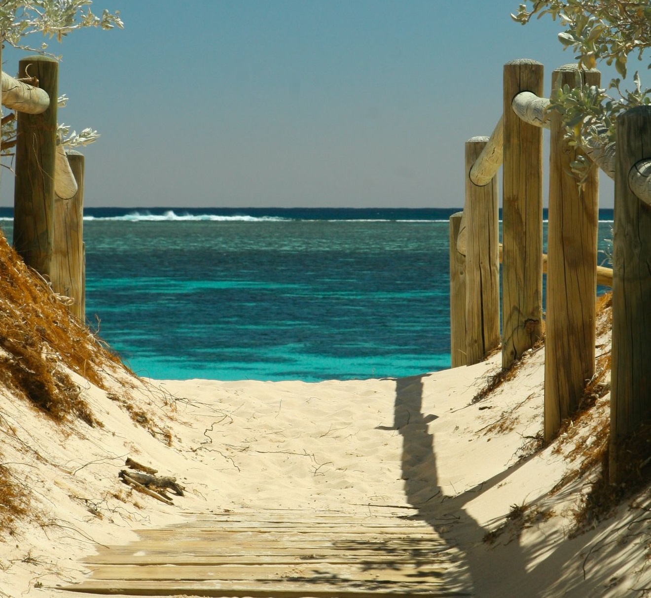 Sandiger Weg zum Meer. Links und Rechts ist ein Holzpfahl Zaun