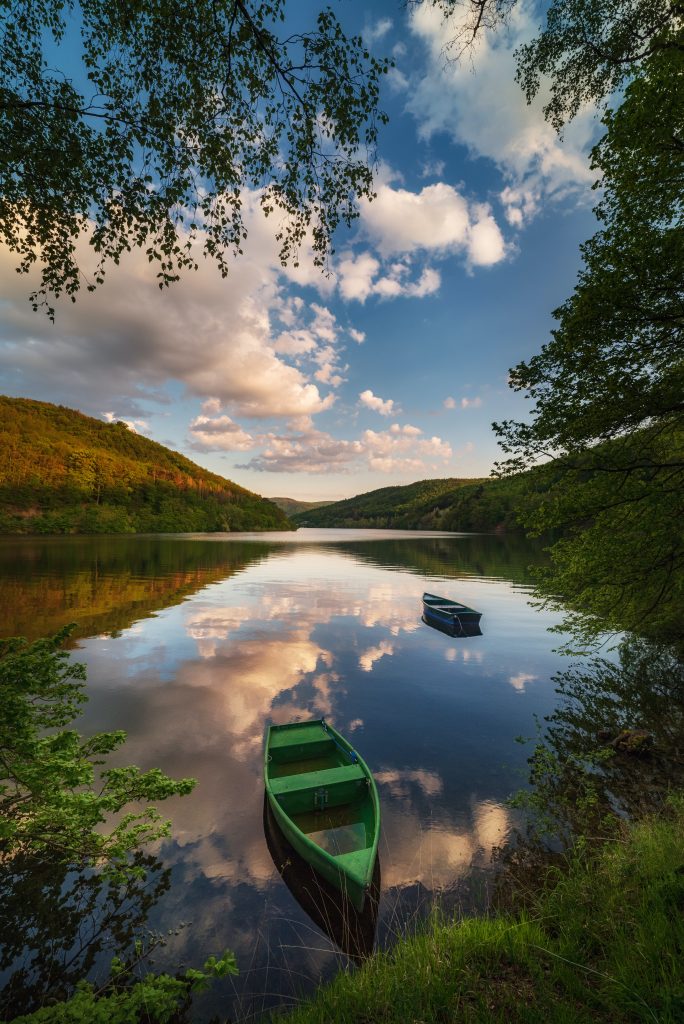 Camping Sauerland - zwei kleinen Ruderboote auf einem See welcher von Wald umrandet ist 