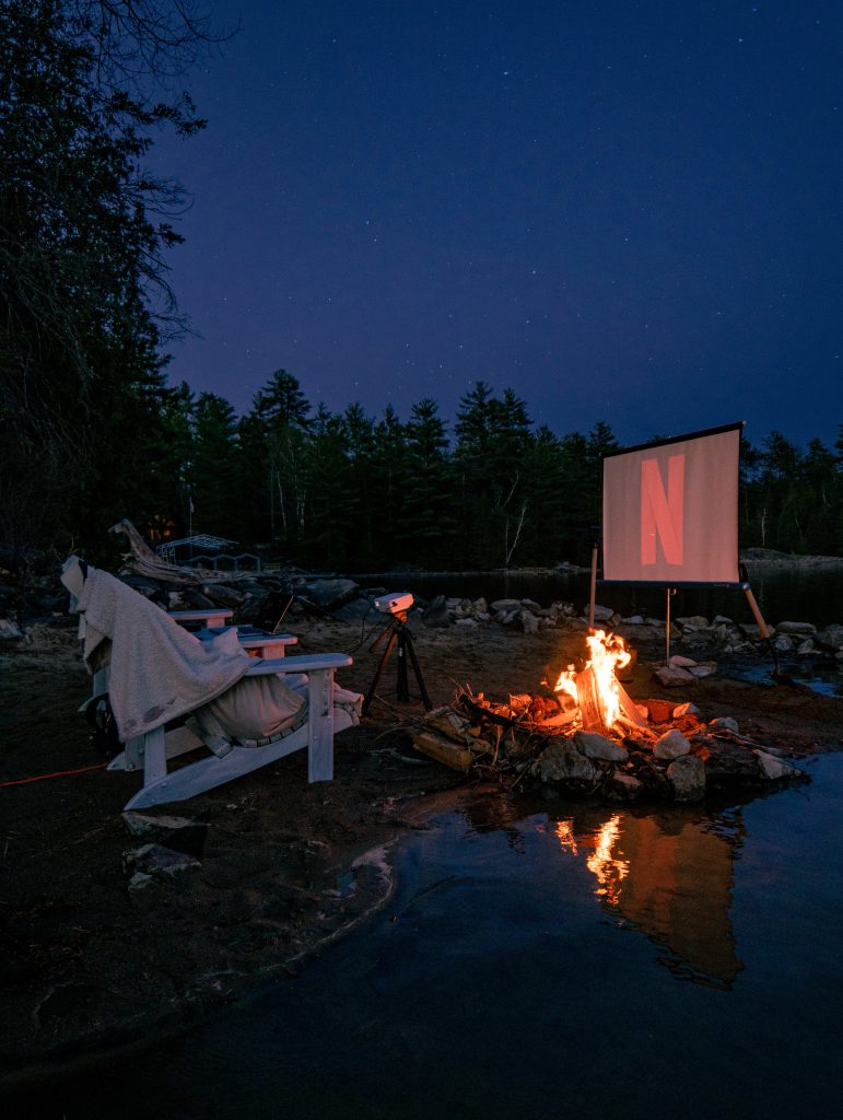 Bester WLAN-Router für Wohnmobil - Blick auf zwei Campingstühle bei Nacht an  einem See. Vor den beiden Campingstühlen steht einen Leinwand und man sieht das Netflix Logo 