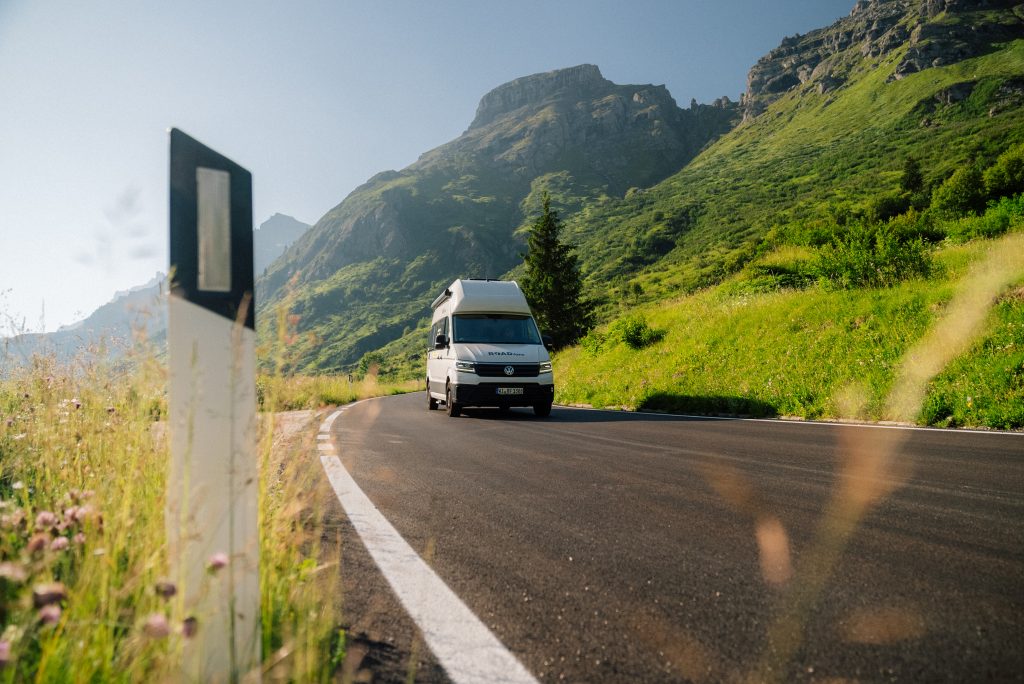 Glamping Allgäu - Blick auf ein fahrendes Wohnmobil von ROADfans mit Bergen im Hintergrund.