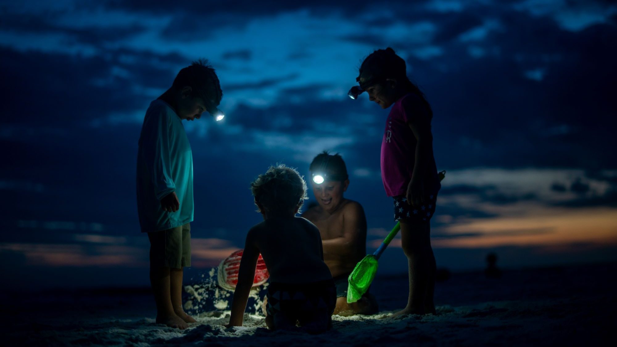 Mehrere Kinder buddeln am Strand. Es ist Nacht.