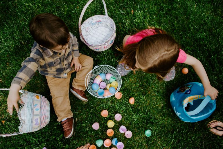 Zwei Kinder sitzen auf einer Wiese mit Körben und Ostereiern