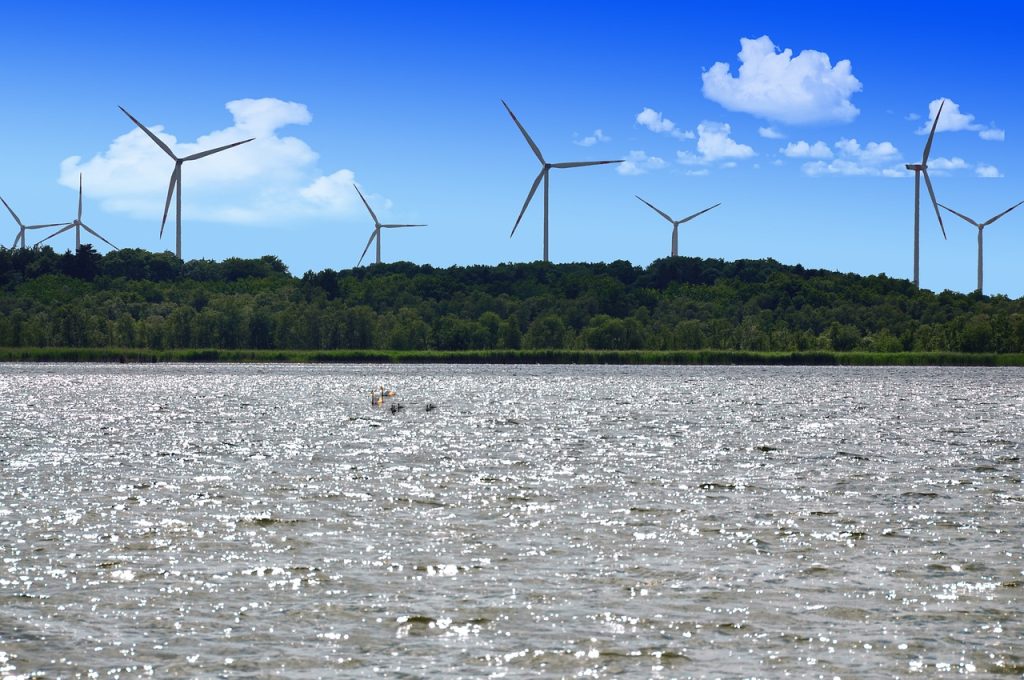 Camping Mecklenburgische Seenplatte - Blick auf den Plauer See mit Wäldern und Windrädern im Hintergrund.