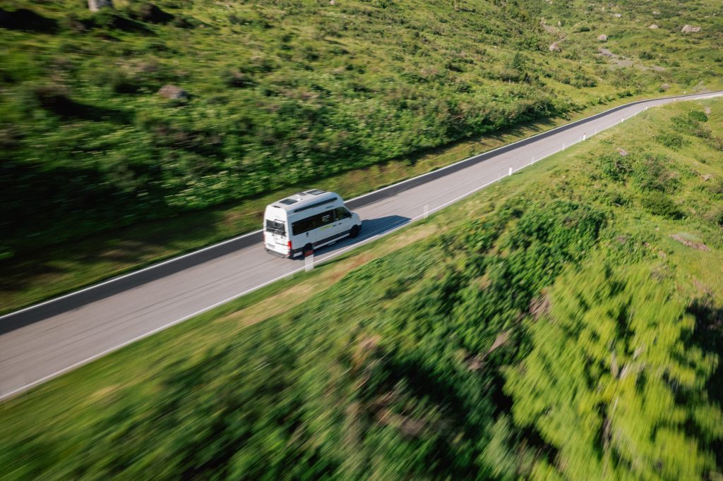 Camping Trends 2024 - Blick auf ein auf der Straße fahrendes Wohnmobil zwischen grüner Umgebung.